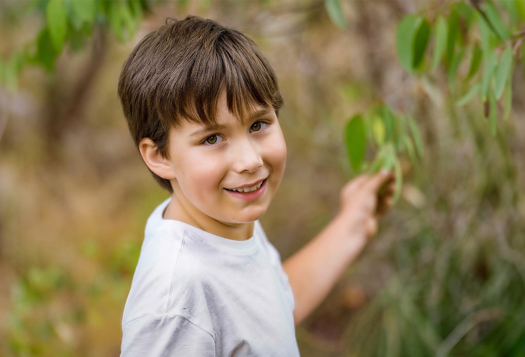 Young boy smiling among gum tree leaves in outdoor portrait, Perth children's photographer Fisher Photography
