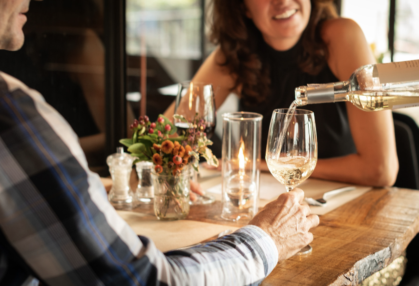 A server pours chilled white wine for a couple during a romantic candlelit dinner date at a rustic restaurant.