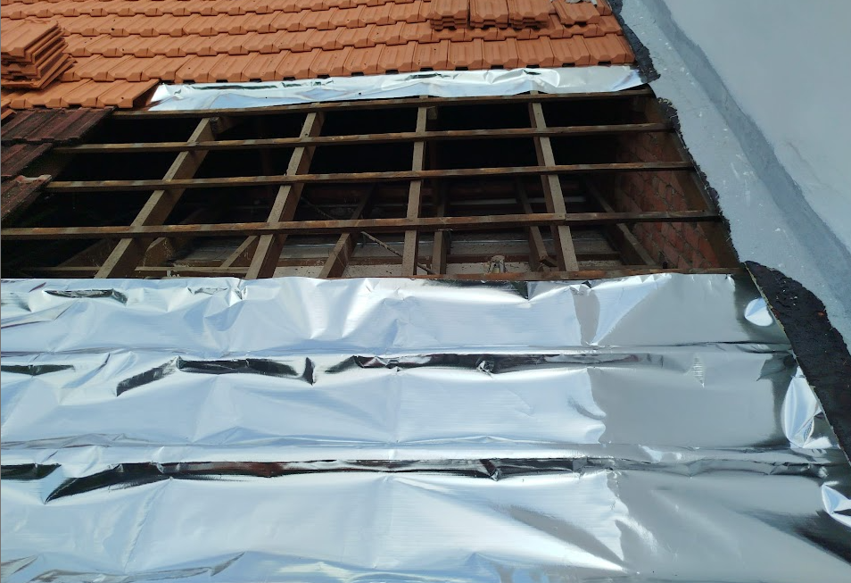 A roof repair project showing exposed wooden battens and reflective foil insulation under terracotta tiles.