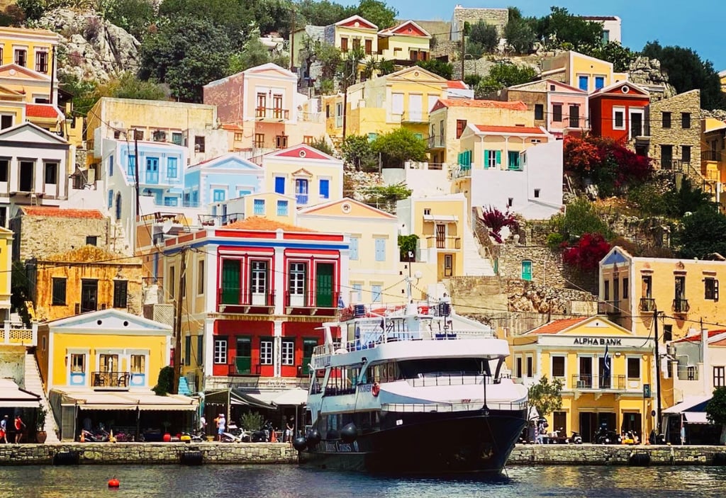 Colorful neoclassical houses on a hillside overlooking a ferry at Symi Island harbor in Greece.