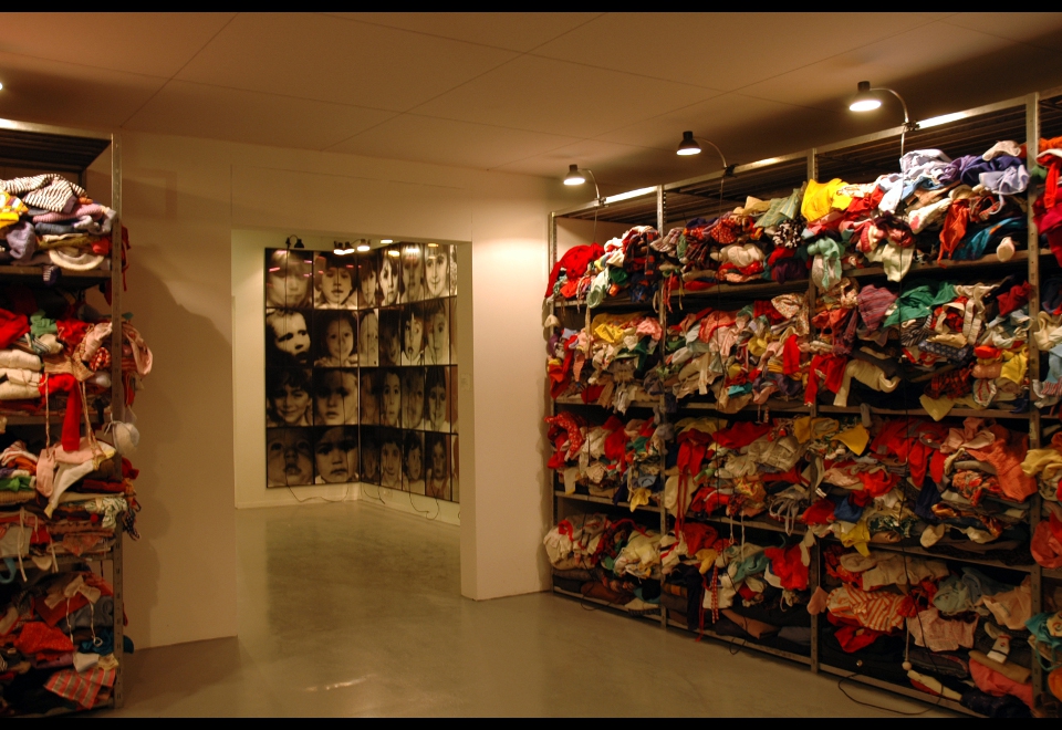 Christian Boltanski art installation featuring stacks of used clothing and a grid of children's portraits.