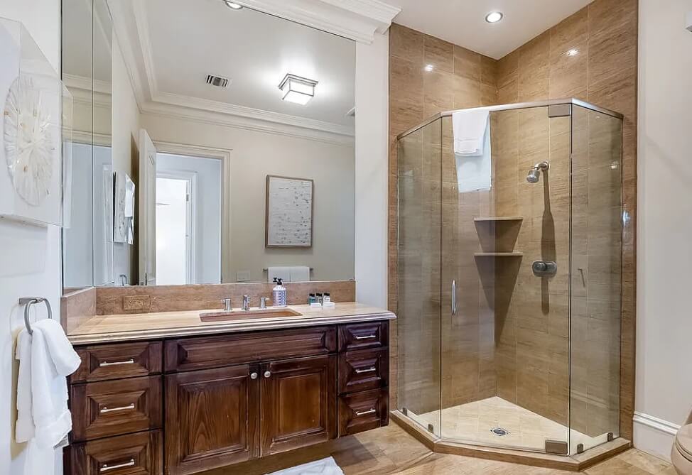 Bathroom remodel with a wood vanity, stone countertop, and glass-enclosed shower.