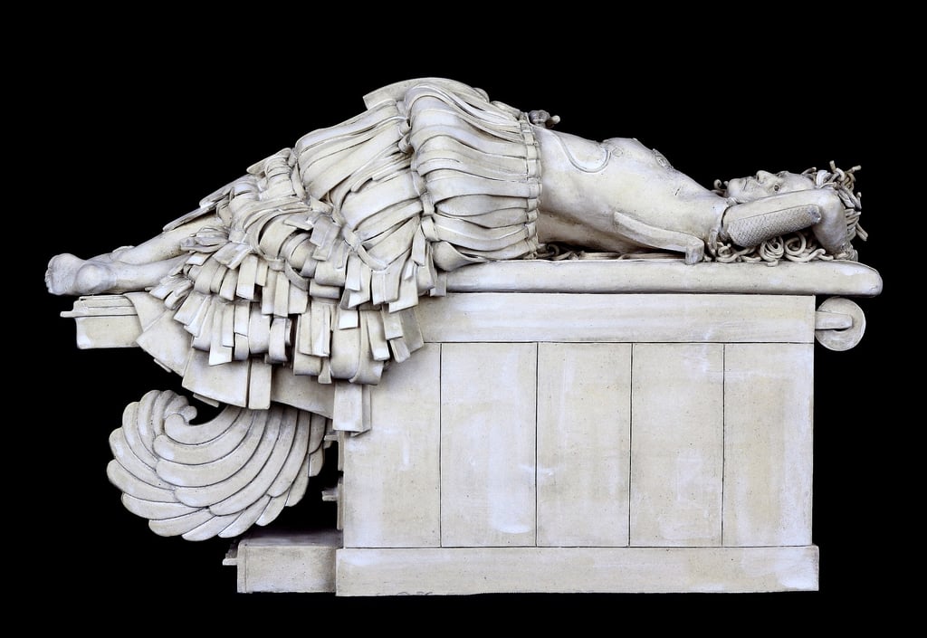 Ceramic sculpture of woman with feathered tail on examination table after breast reconstruction.