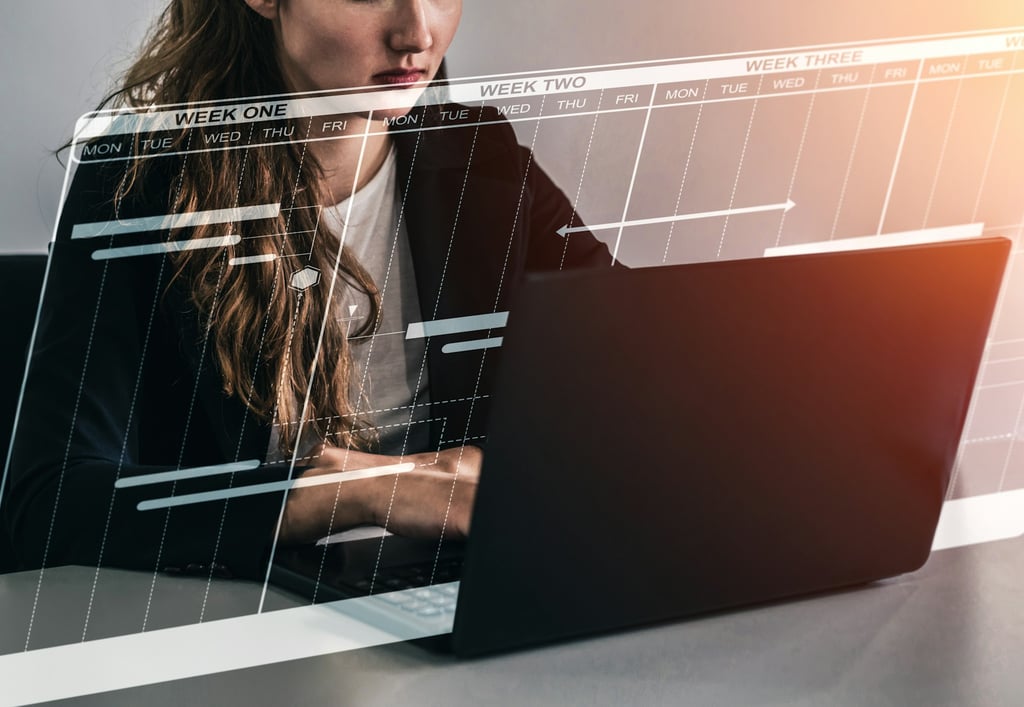 a woman sitting at a desk with an open laptop, working on a calendar