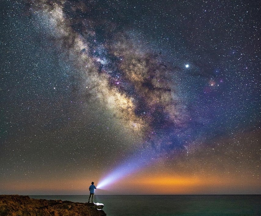 Galaxy of starts in night sky with lone man holding flashlight