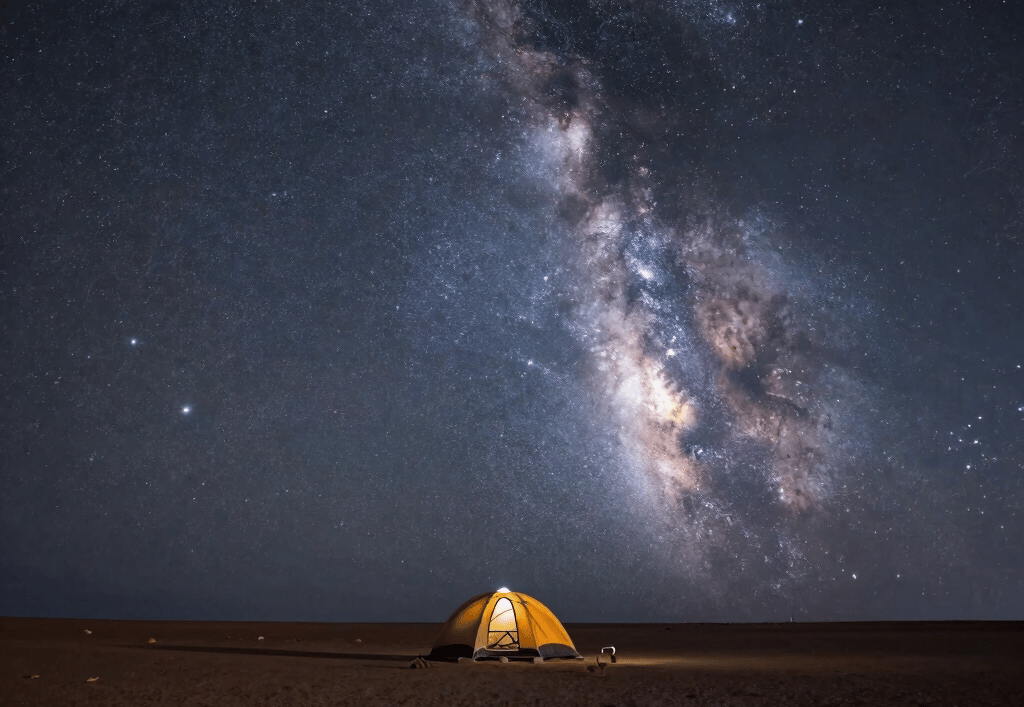 A glowing yellow camping tent under a vibrant Milky Way galaxy night sky in the desert.