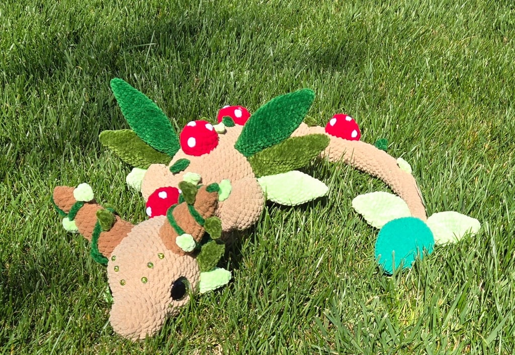 “Handmade crochet forest dragon plushie with antlers, felt leaves, and red mushroom details, resting