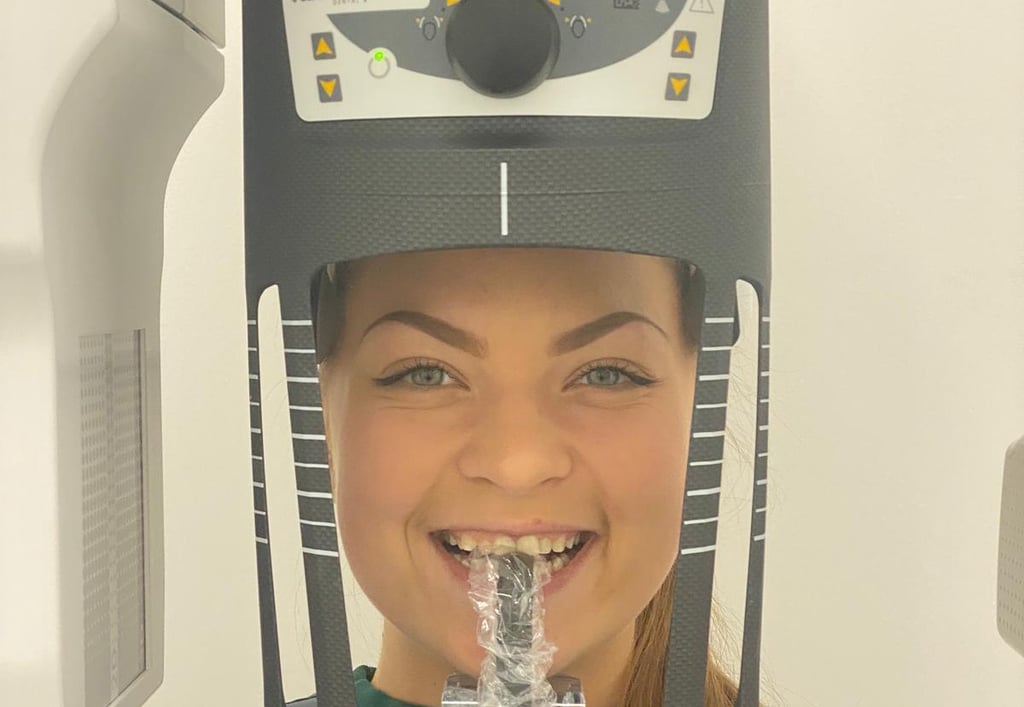 A smiling dental patient positioned in a Carestream CS 8100 3D cone beam CT scanner for a diagnostic panoramic x-ray.