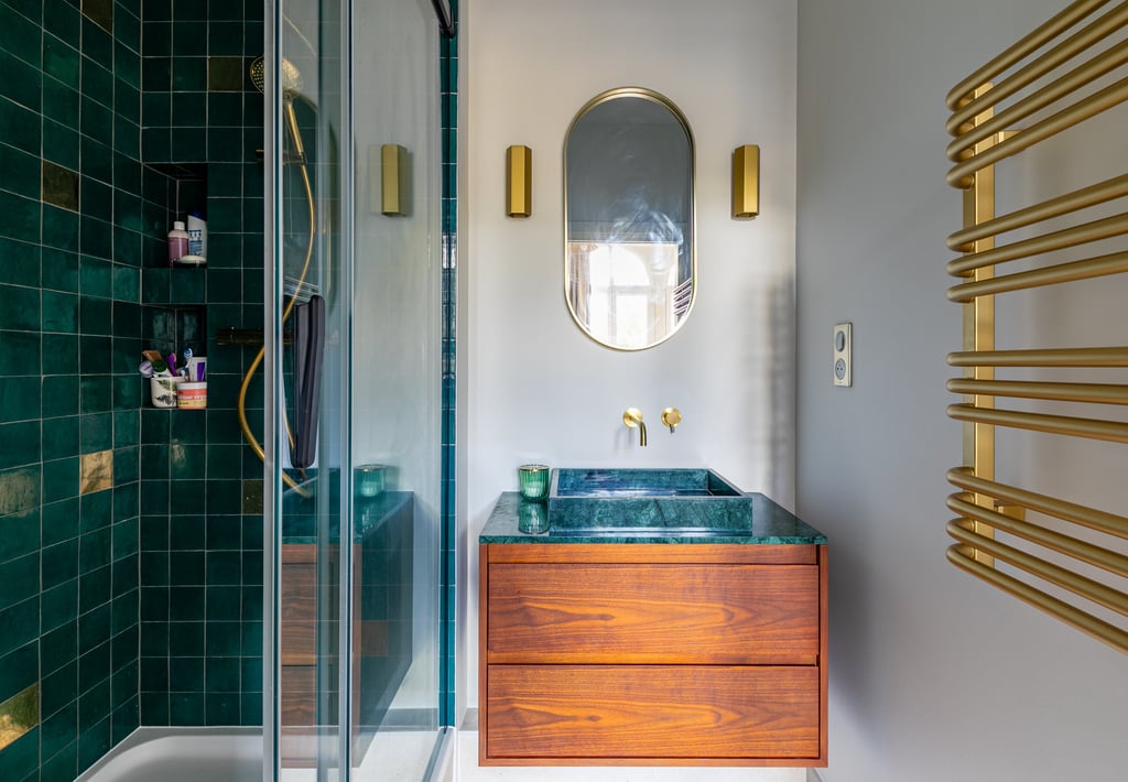 Modern bathroom with green tiles, wood vanity, gold fixtures, and a heated towel rack.