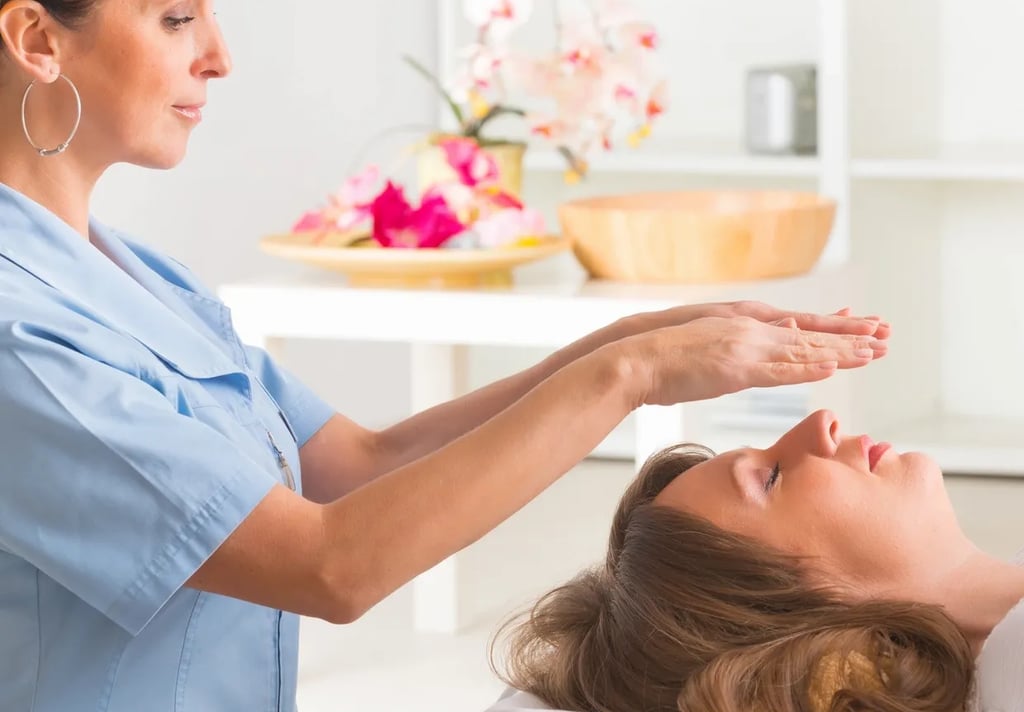 A standing ReikiPractitioner hovers her hands above a woman's face who is laying down