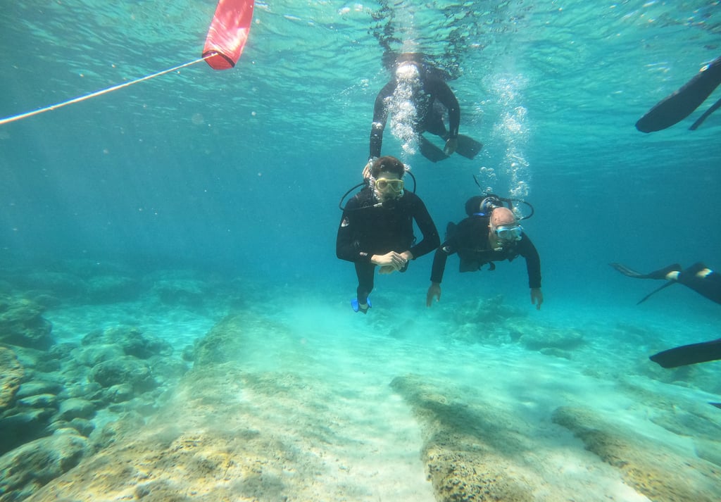 Scuba divers exploring a tropical coral reef in clear blue ocean water during a guided diving tour.