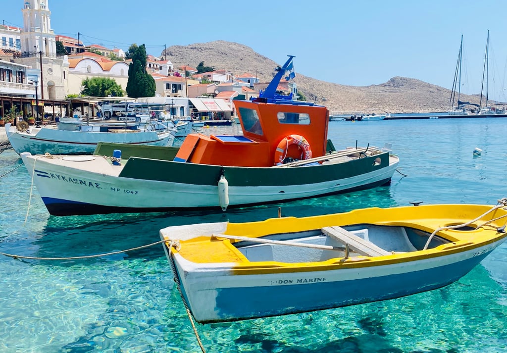 Traditional fishing boats floating on clear turquoise water at the scenic harbor of Halki Island in Greece.