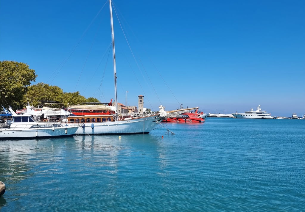 Luxury yachts and sailboats anchored in the sunny Mandraki Harbor of Rhodes, Greece.