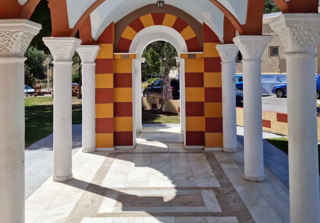 Greek Orthodox church arcade with white marble columns and arched hallways in a sunny courtyard.