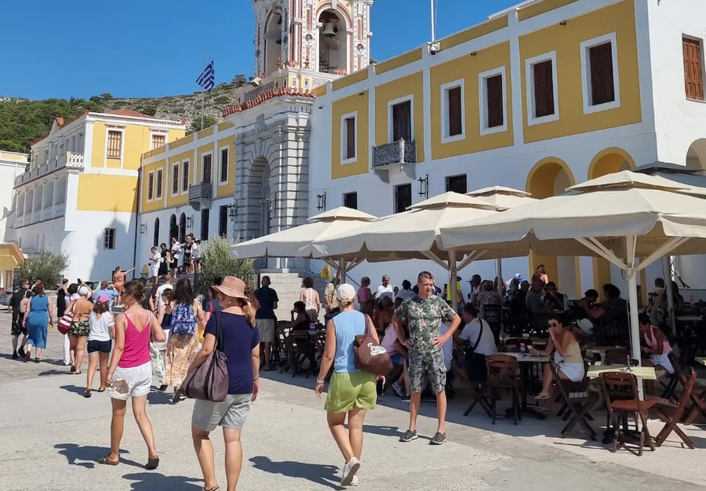 Panormitis Monastery clock tower and courtyard with tourists on Symi Island, Greece.