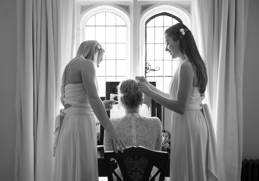 black & white photo of bridesmaids helping bride get ready, they are in front of a large window, curtains are framing them