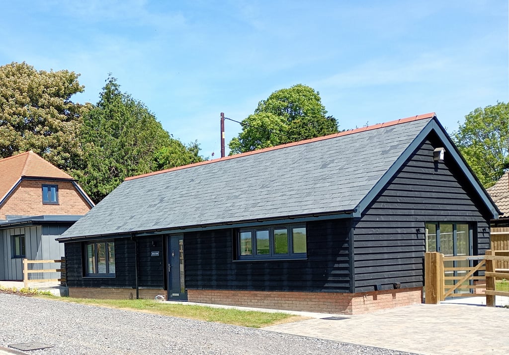 Modern black timber barn conversion with slate roof and gravel driveway in a rural setting.