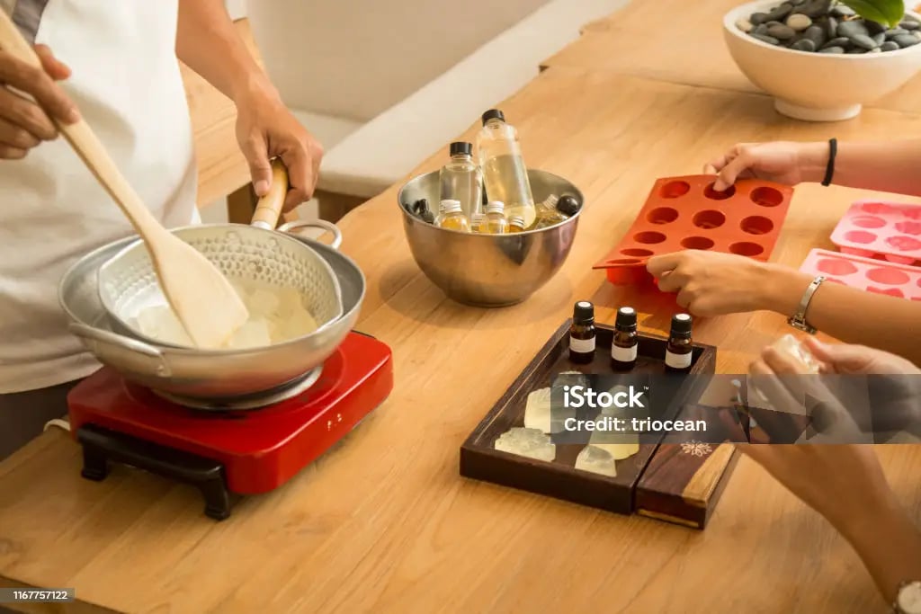 Handmade soap making workshop with essential oils, silicone molds, and melting glycerin soap base.