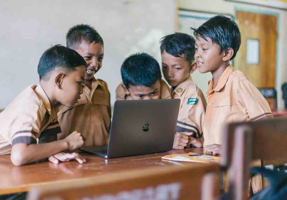 a group of children in school uniforms looking at a laptop