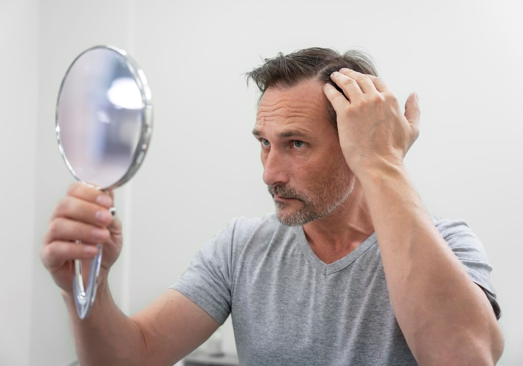 a man with a, holding a mirror and looking at his hair