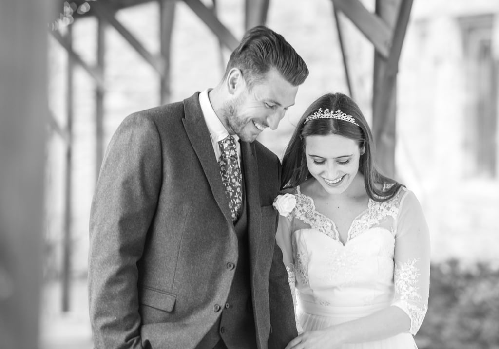 zoomed in black and white photo of bride and groom walking both laughing and smiling, archway framing them 