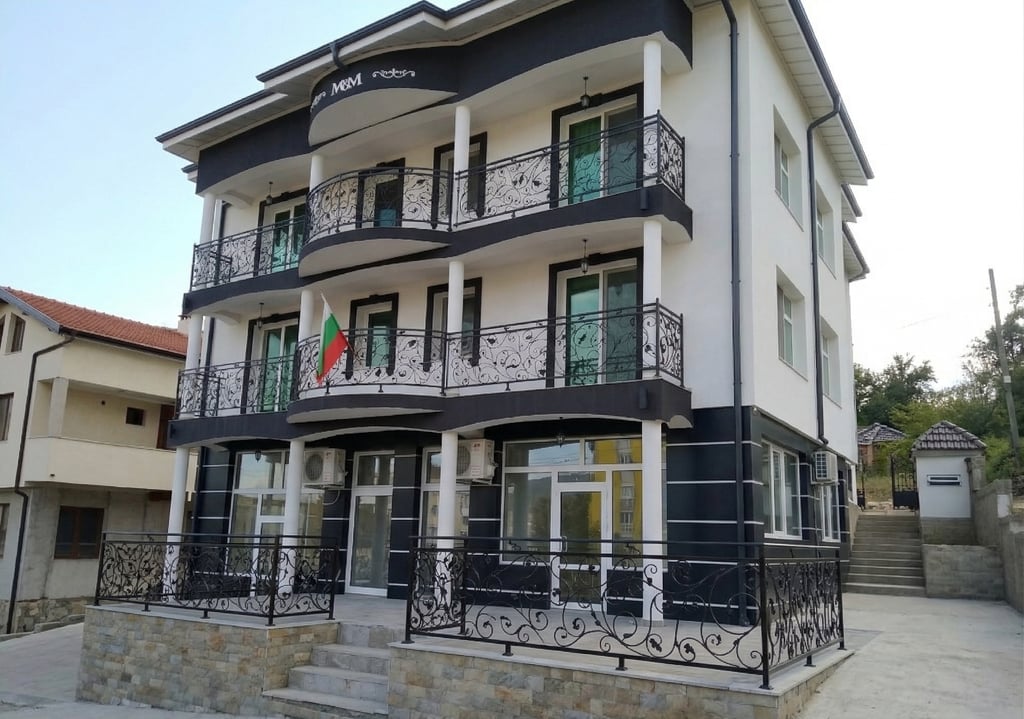 Modern white and black three-story apartment building with ornate wrought iron balconies and a Bulgarian flag.
