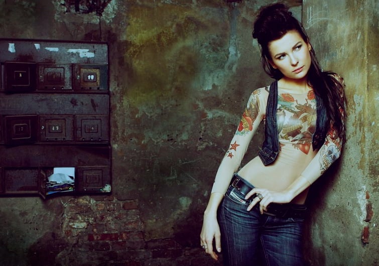 Audrius Turskas photography a woman with tattoos on her chest standing next to old textured wall