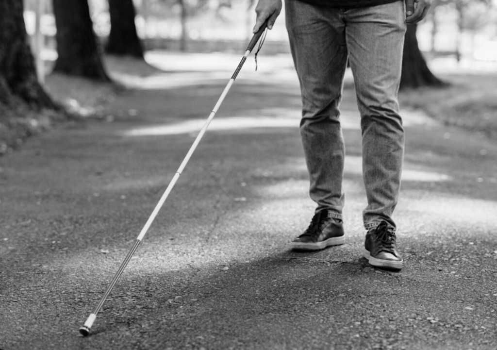 Niewidomy mężczyzna porusza się za pomocą białej laski w ścieżce.