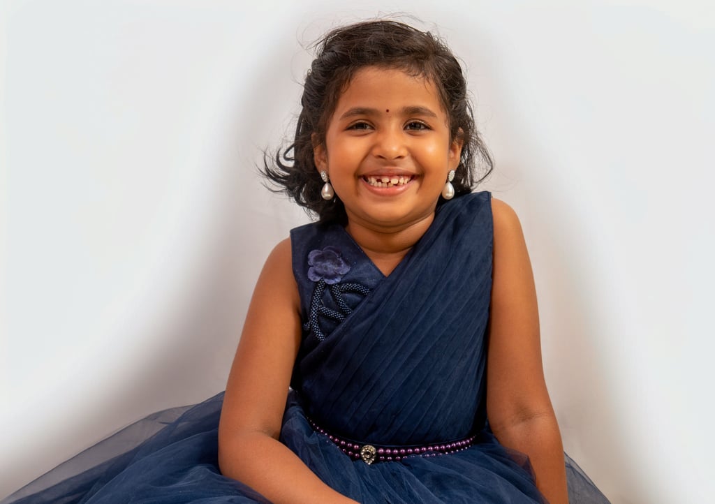 a young girl in a blue dress smiling and holding a cake