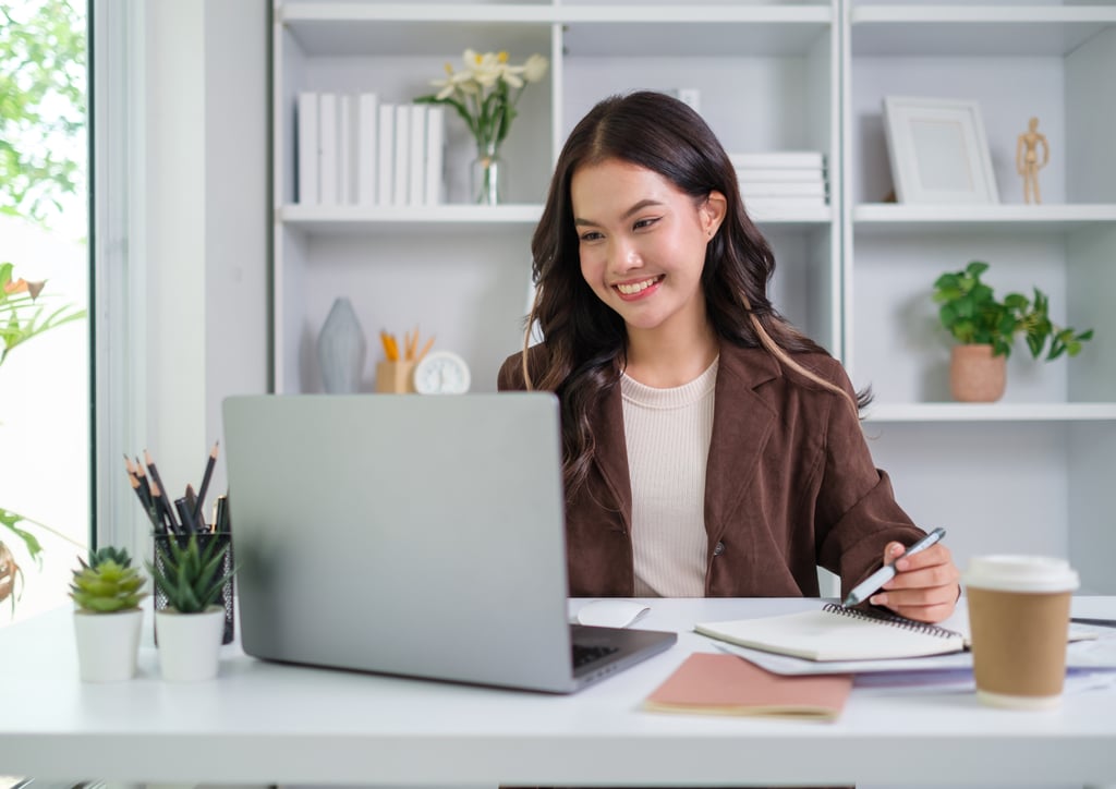 Chica sonriente sentada en un escritorio con un ordenador portátil y una libreta