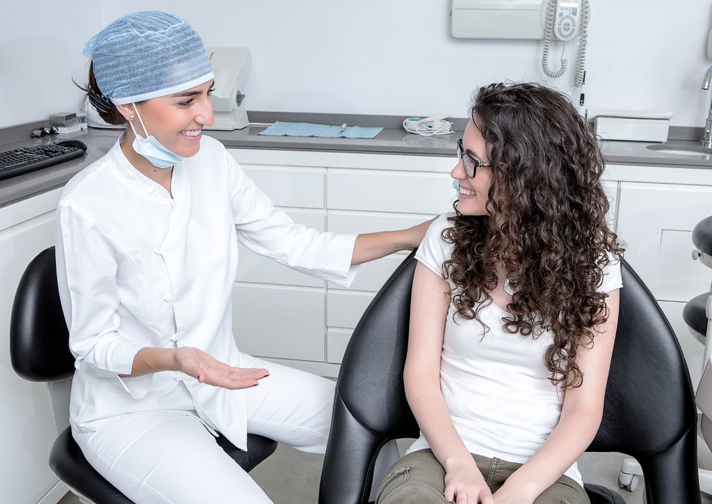 una mujer con camisa blanca y un dentista con bata blanca en una clínica dental