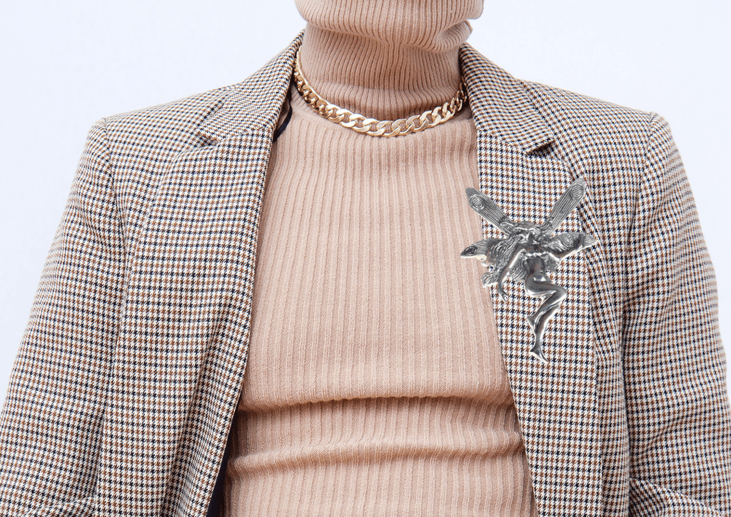 Vintage silver fairy brooch pinned to a brown plaid blazer with a beige turtle neck