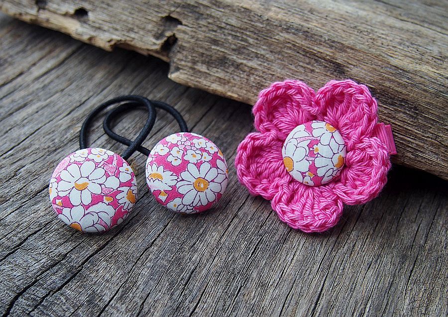 różowy zestaw gumek do włosów i spinki z kwiatkiem na tle drewnianej deski