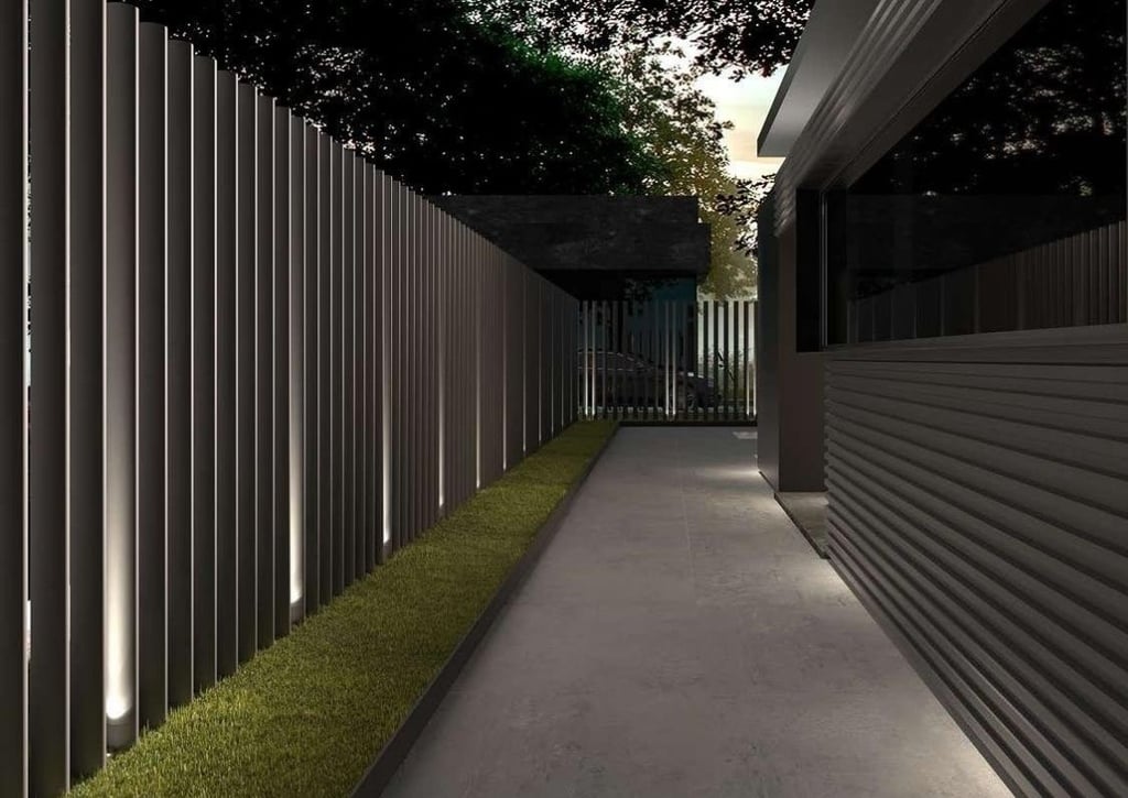 Camino peatonal flanqueado por valla metálica contemporánea con iluminación ambiental