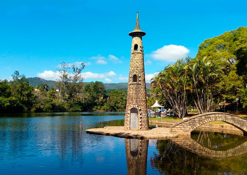 a clock tower in a park with a bridge over a river