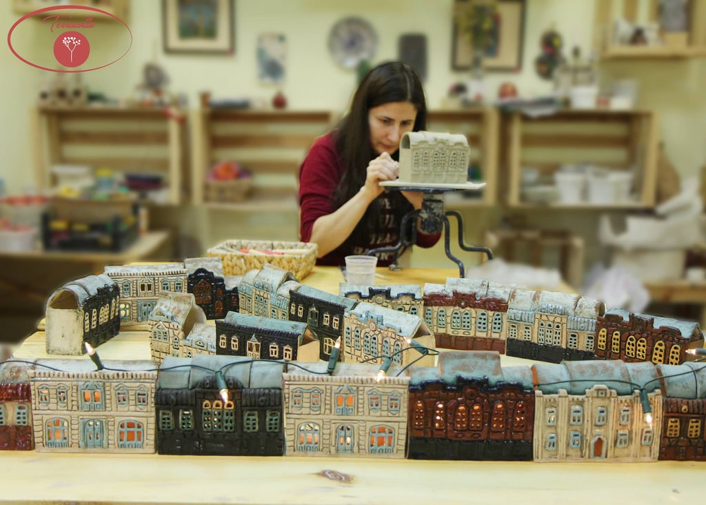 A ceramic artist handcrafting miniature clay houses and glowing ceramic city buildings in a pottery studio.