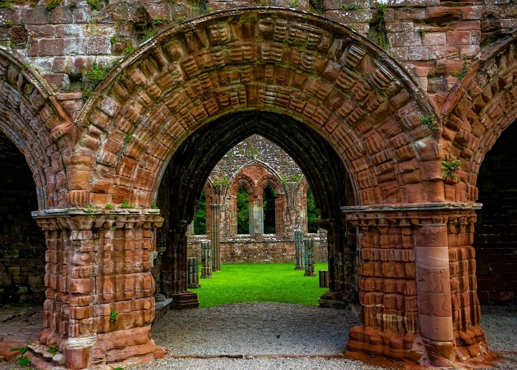 Ornate Romanesque stone archway at the historic Sweetheart Abbey ruins in Scotland.