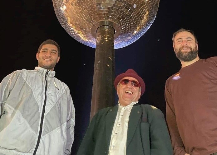 Three men smiling beneath the Sunsphere tower at night in Knoxville World's Fair Park.