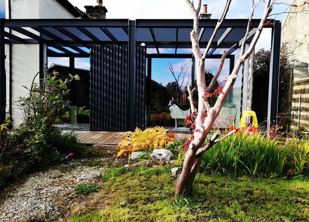 Modern black timber slat garden room extension with sliding doors and wooden decking.