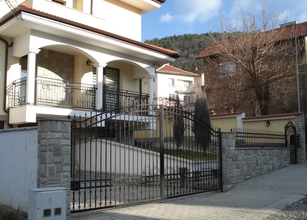 Modern white house with a decorative wrought iron gate and stone pillar fencing.