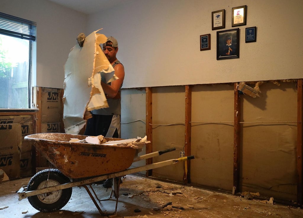 A worker removing damaged drywall debris into a wheelbarrow during a home interior demolition and renovation.