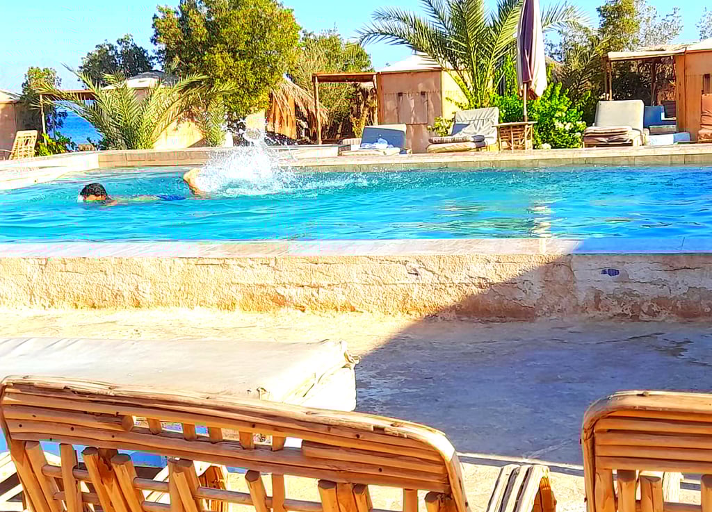 Дечак који плива у базену близу мора и бунгалова у бедуинској звезди Египат