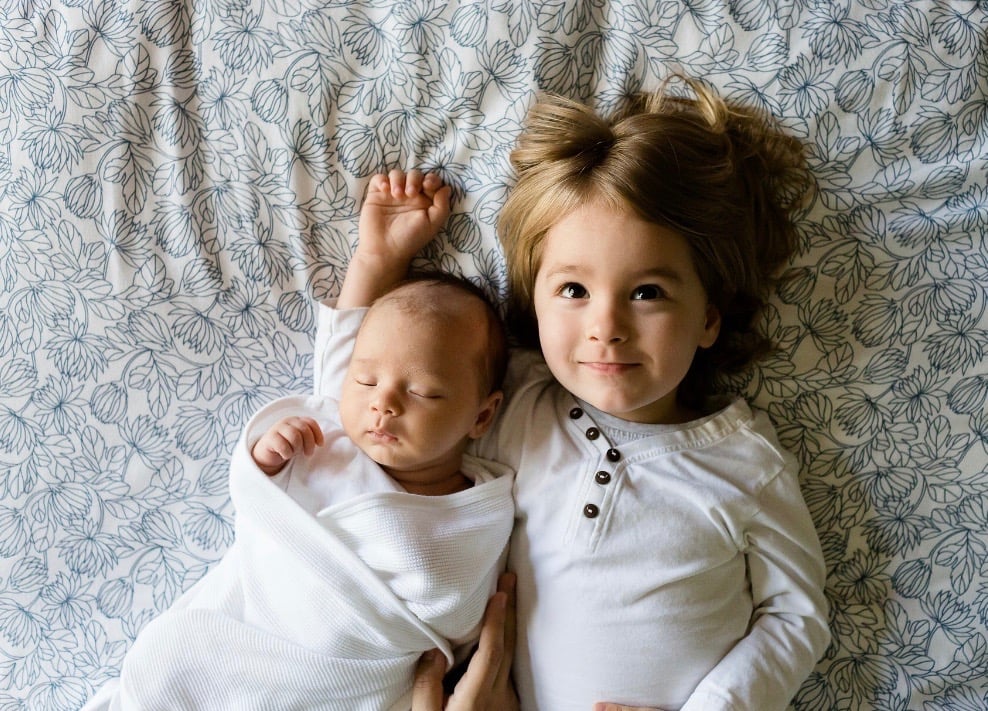 sleeping baby and older sister lying on bed