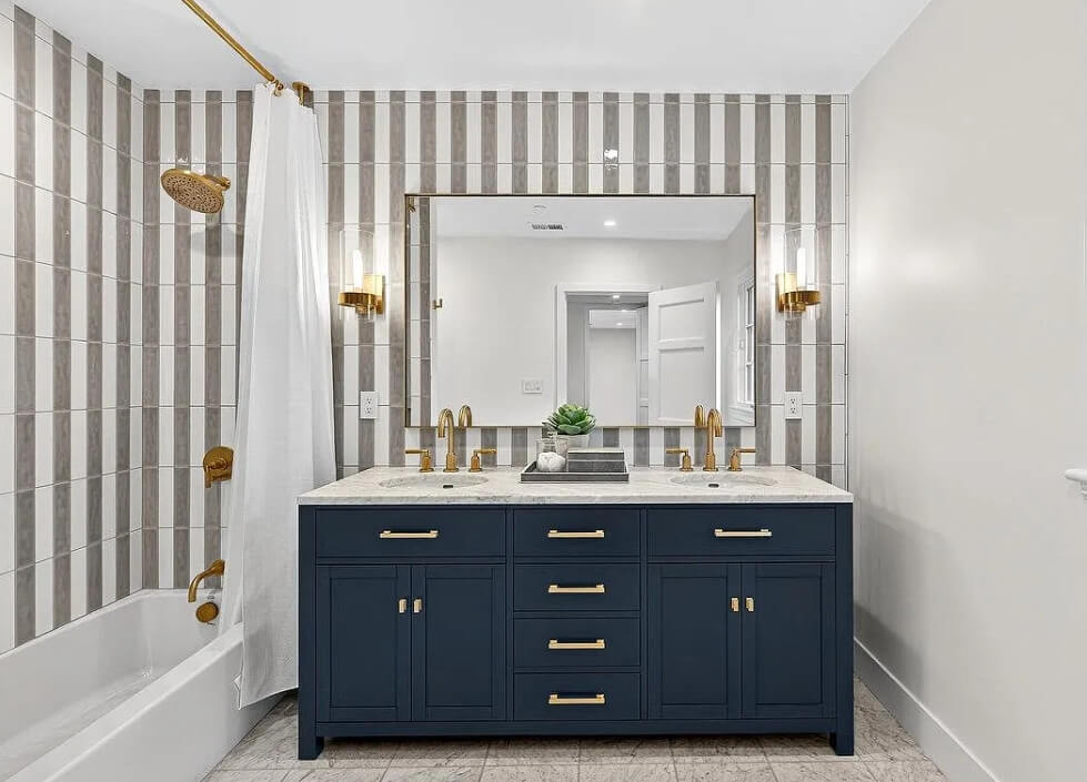 Bathroom remodel with a blue vanity, gold fixtures, and striped tile walls.