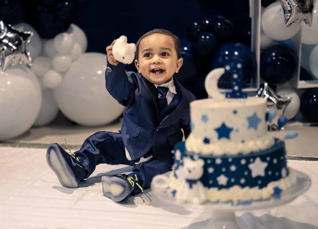 a baby boy in a suit and tie, sitting next to a birthday cake
