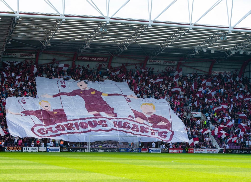 Innenansicht des Tynecastle Park in Edinburgh: dicht gefüllte Tribünen mit jubelnden Fans, rot-weißen Vereinsfarben, klar erk