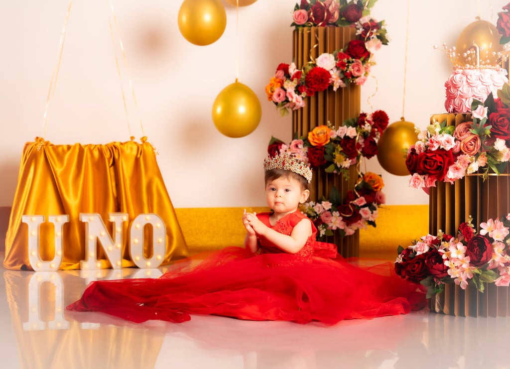 a baby girl in a red dress sitting on a floor