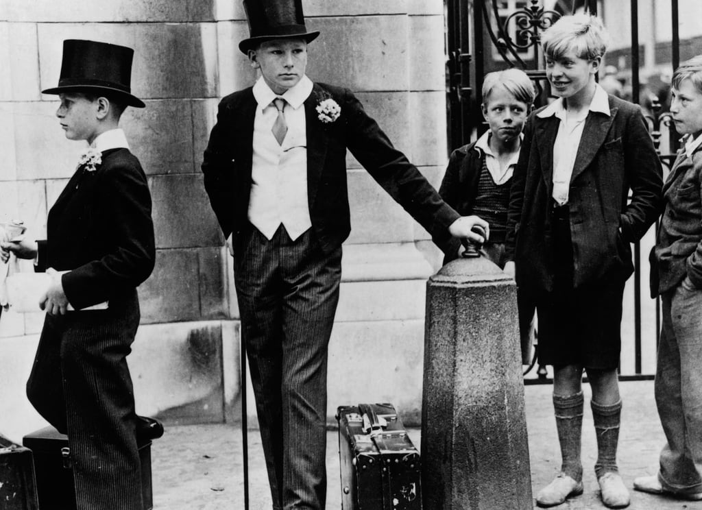 Local boys look on as two Harrow schoolboys wait outside Lord’s cricket ground