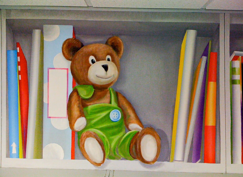 A painted bookshelf in trompe l'oeil style, showing a cute stuffed bear and fun colourful books