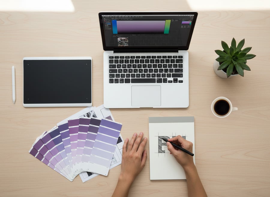 Scrivania di una graphic designer che lavora a una brand identity con palette colori, laptop e bozze